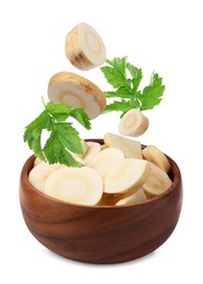 Pieces of parsnip root and leaves falling into wooden bowl on white background