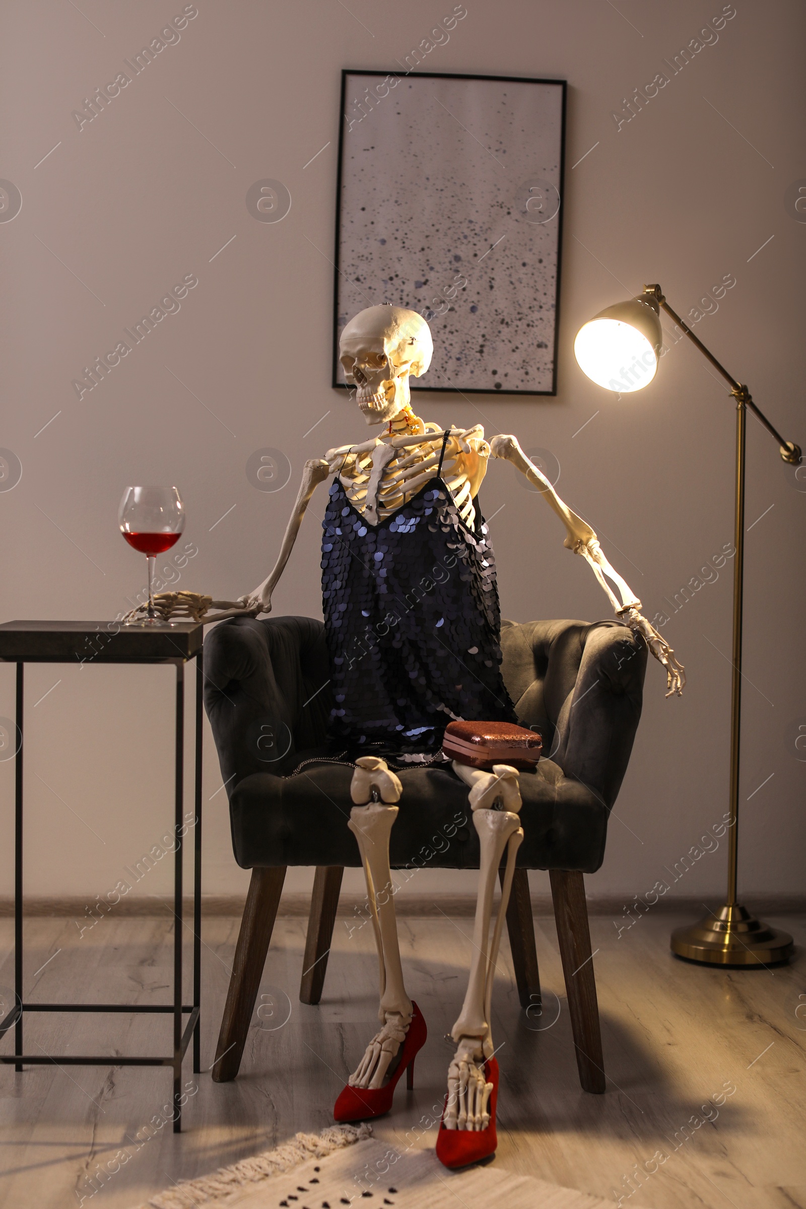 Photo of Skeleton in dress with wine sitting at table indoors