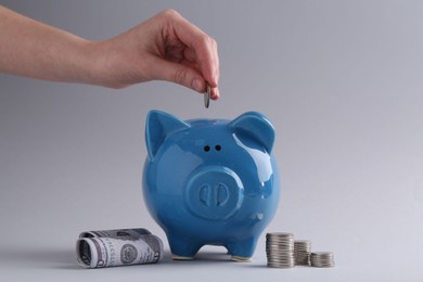 Photo of Financial savings. Woman putting coin into piggy bank on grey background, closeup