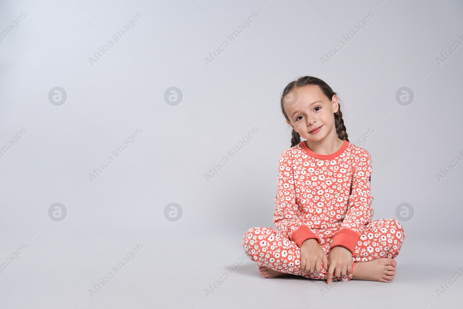 Photo of Cute girl in pajamas with floral pattern on light grey background. Space for text