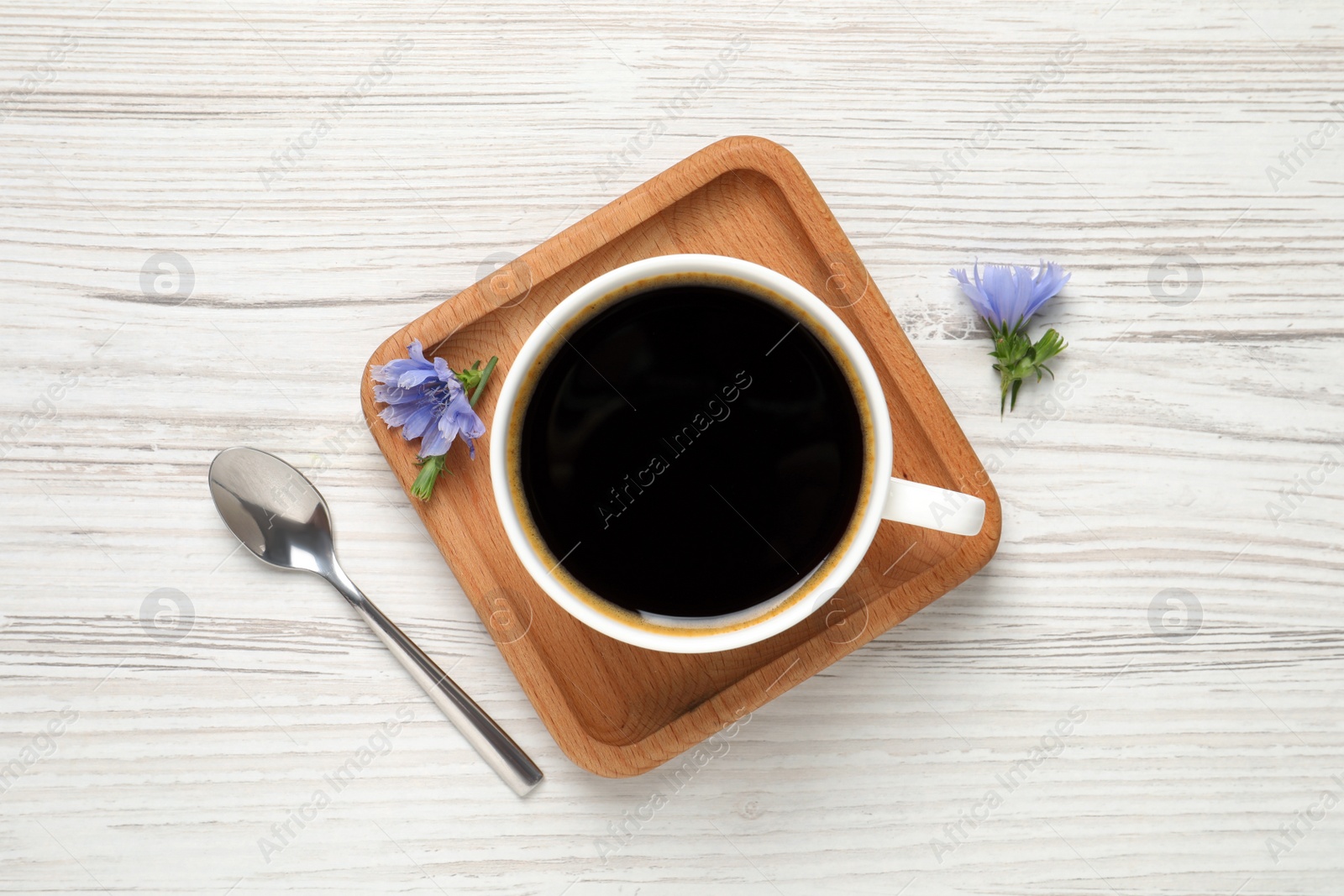 Photo of Cup of delicious chicory drink, spoon and flowers on white wooden table, flat lay
