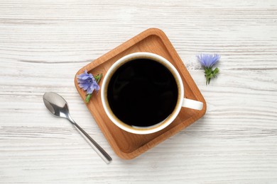 Cup of delicious chicory drink, spoon and flowers on white wooden table, flat lay