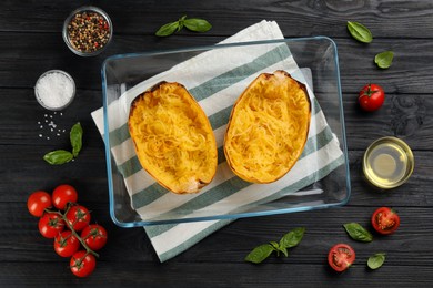 Photo of Halves of cooked spaghetti squash in baking dish and ingredients on black wooden table, flat lay