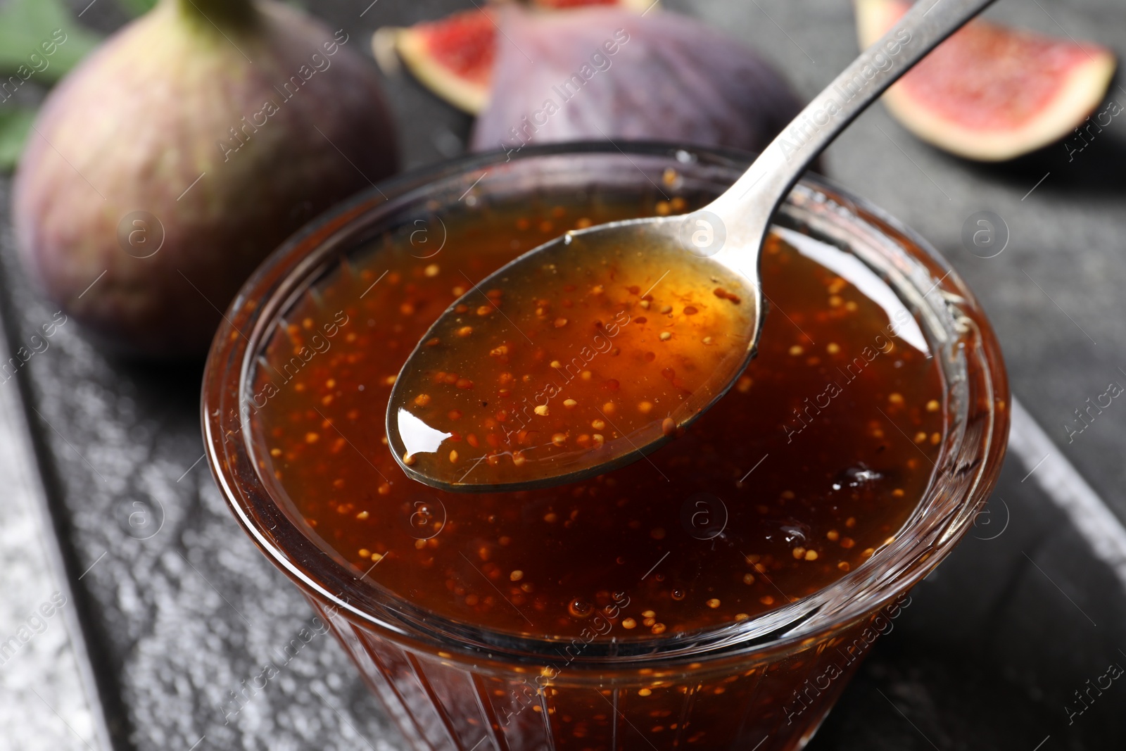 Photo of Glass bowl with tasty fig jam, spoon and fresh fruits on table, closeup