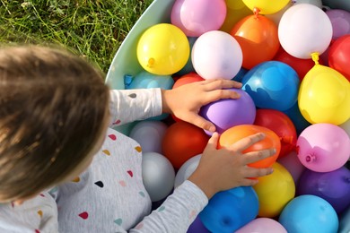 Little girl with basin of water bombs on green grass, top view