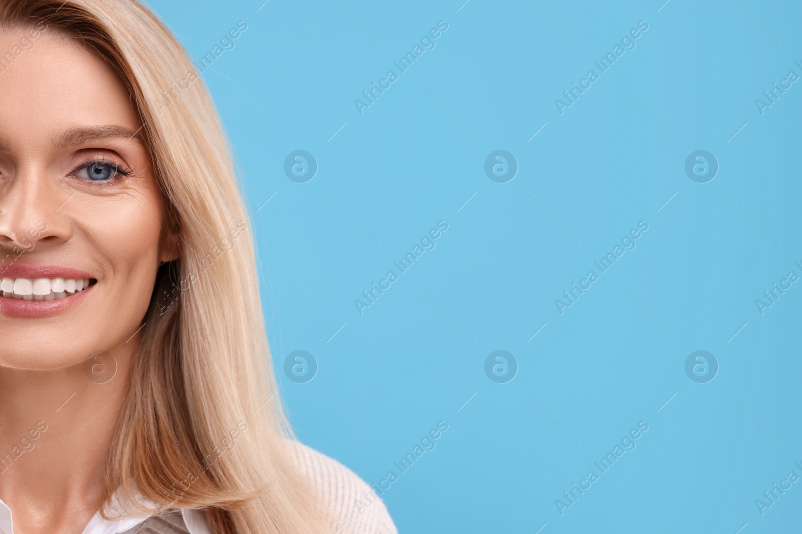 Photo of Portrait of smiling middle aged woman on light blue background, closeup. Space for text