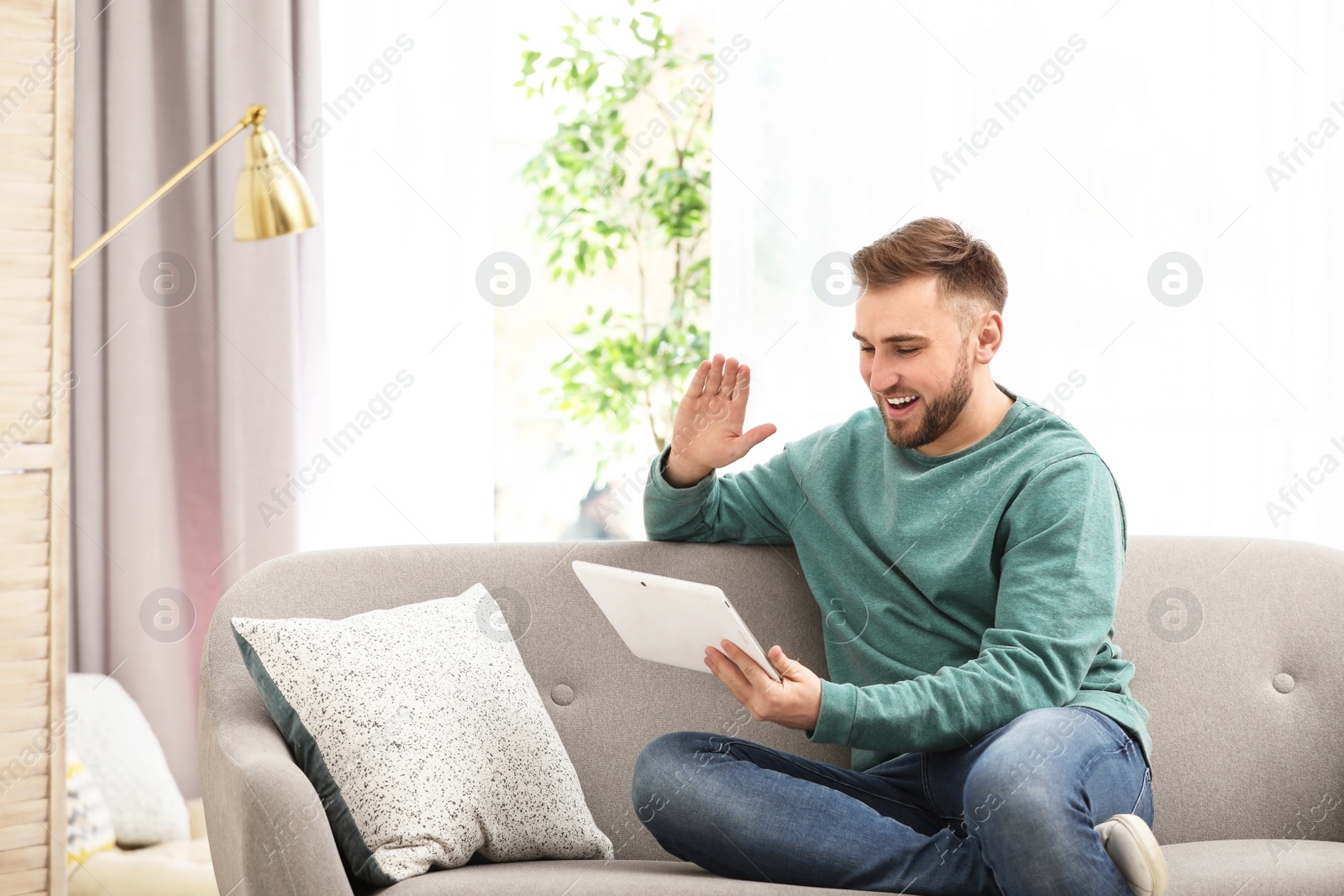 Photo of Young man using video chat on tablet in living room