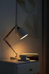 Photo of Stylish lamp, cup of drink and books on table in dark room. Interior design