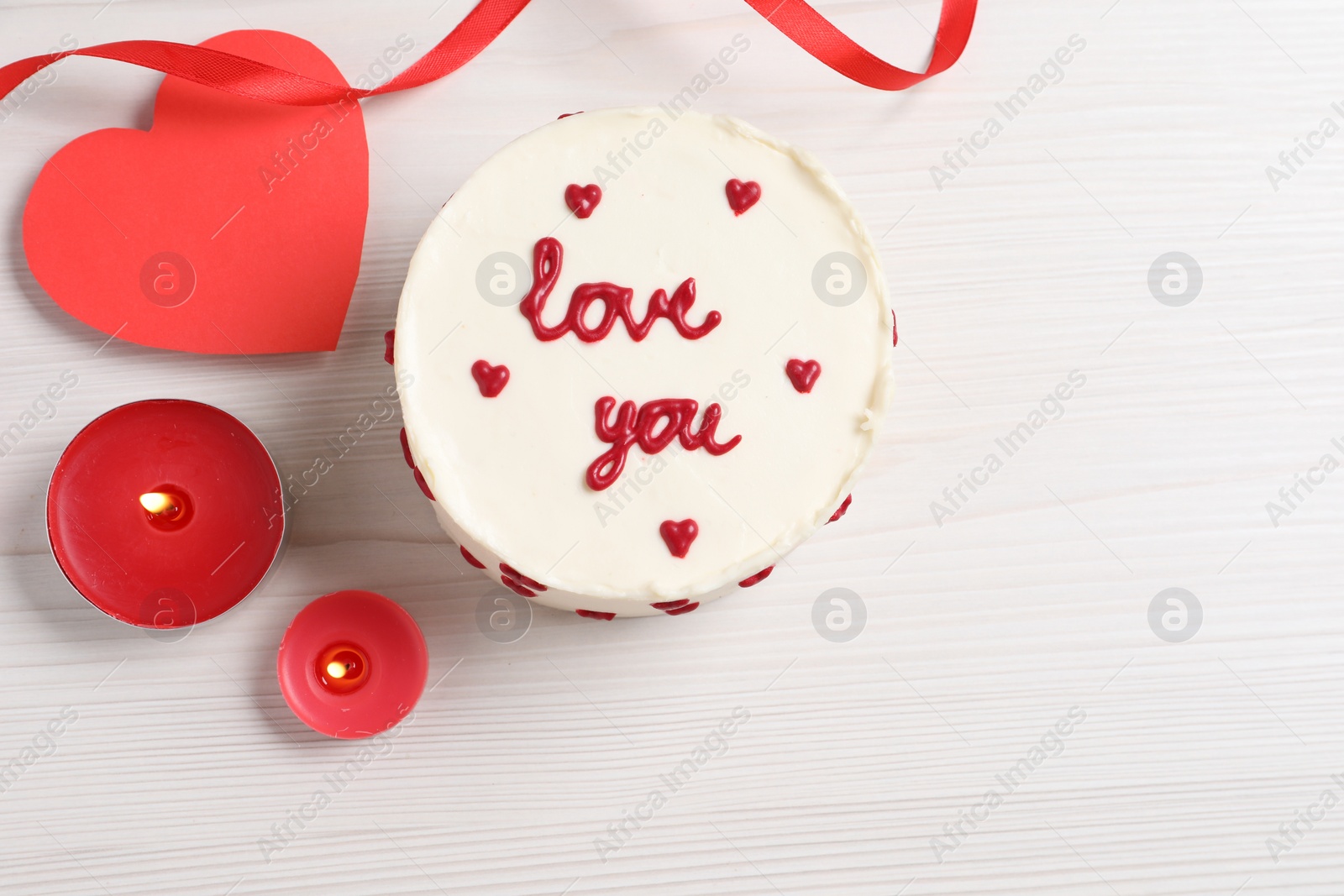 Photo of Bento cake with text Love You, candles, paper heart and space for text on white wooden table, flat lay. St. Valentine's day surprise