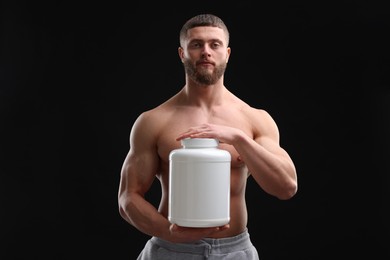 Photo of Young man with muscular body holding jar of protein powder on black background