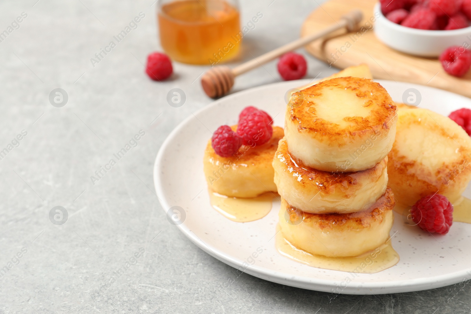 Photo of Delicious cottage cheese pancakes with raspberries and honey on light grey table, space for text