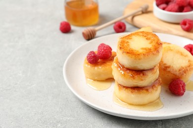 Delicious cottage cheese pancakes with raspberries and honey on light grey table, space for text