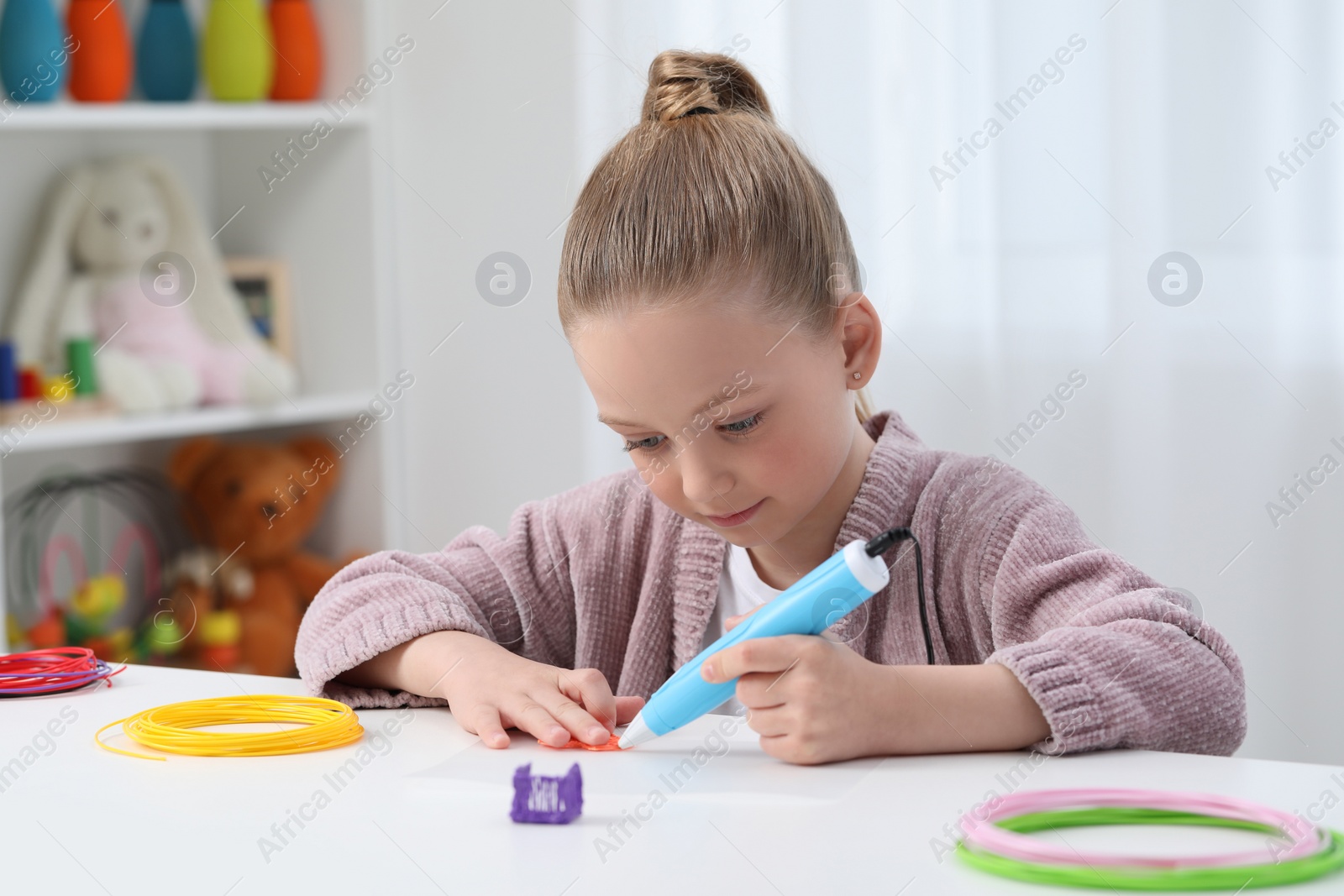 Photo of Girl drawing with stylish 3D pen at white table indoors