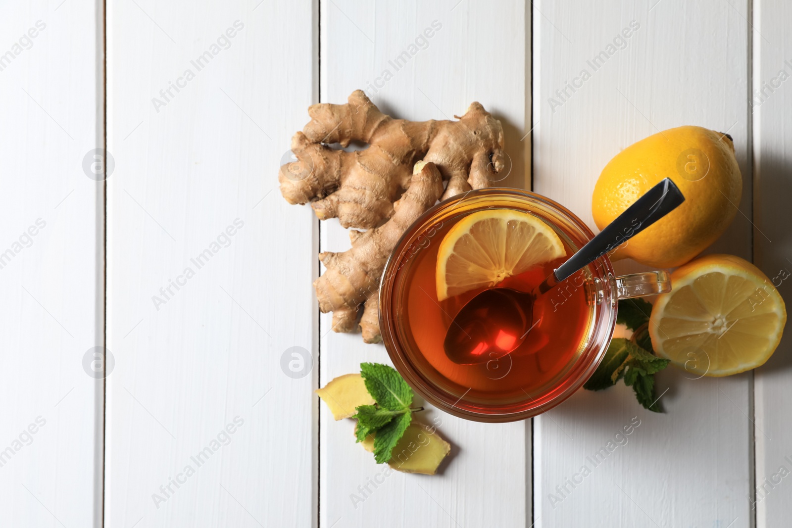 Photo of Cup of delicious tea, ginger roots and lemons on white wooden table, flat lay. Space for text