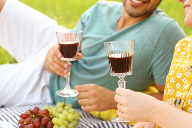 Photo of Young couple with glasses of wine having picnic outdoors, closeup