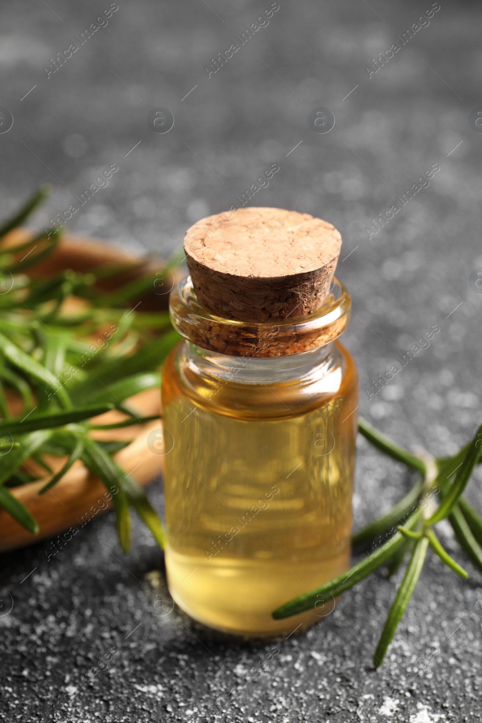 Photo of Bottle with oil and fresh rosemary on grey textured table, closeup