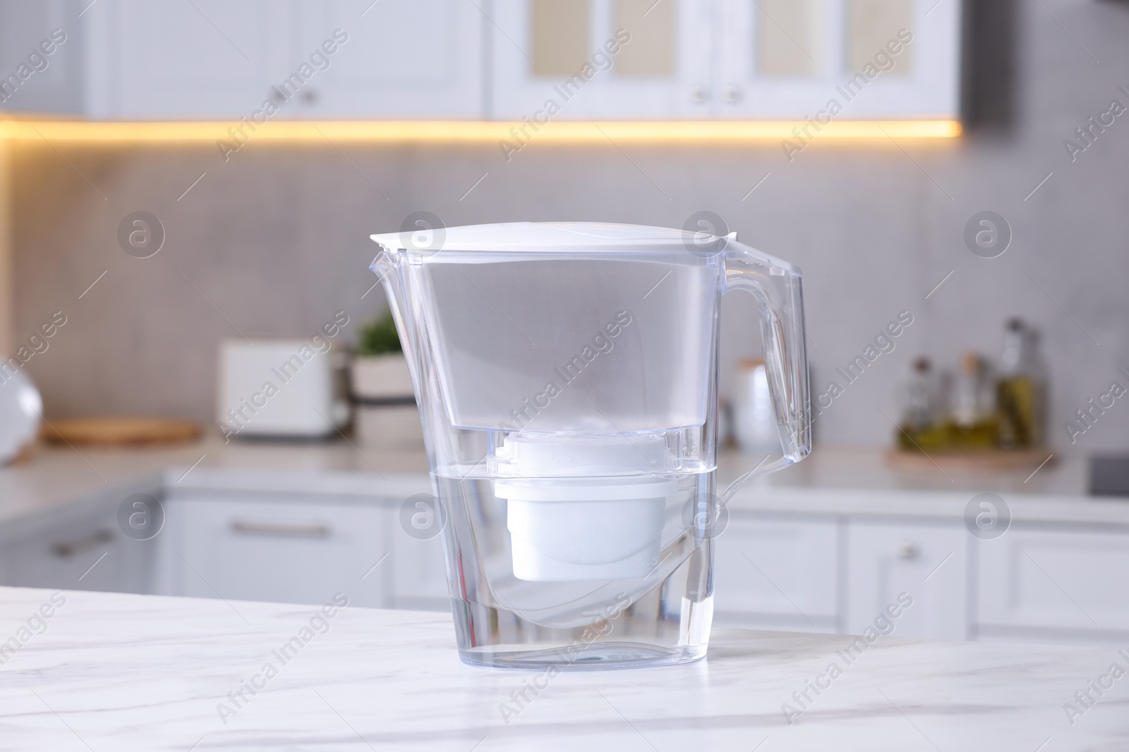 Photo of Water filter jug on white marble table in kitchen, closeup