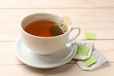 Photo of Tea bags and cup of hot beverage on light wooden table, closeup
