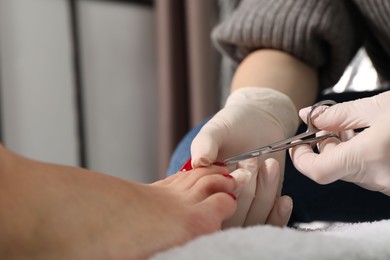 Photo of Pedicurist cutting client`s toenails with scissors in beauty salon, closeup