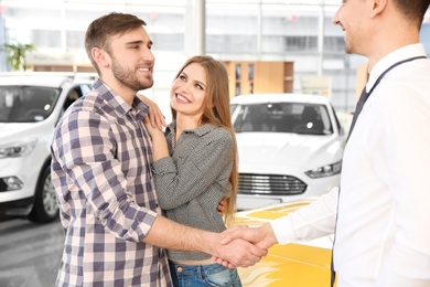 Photo of Young man shaking hands with salesman in car salon