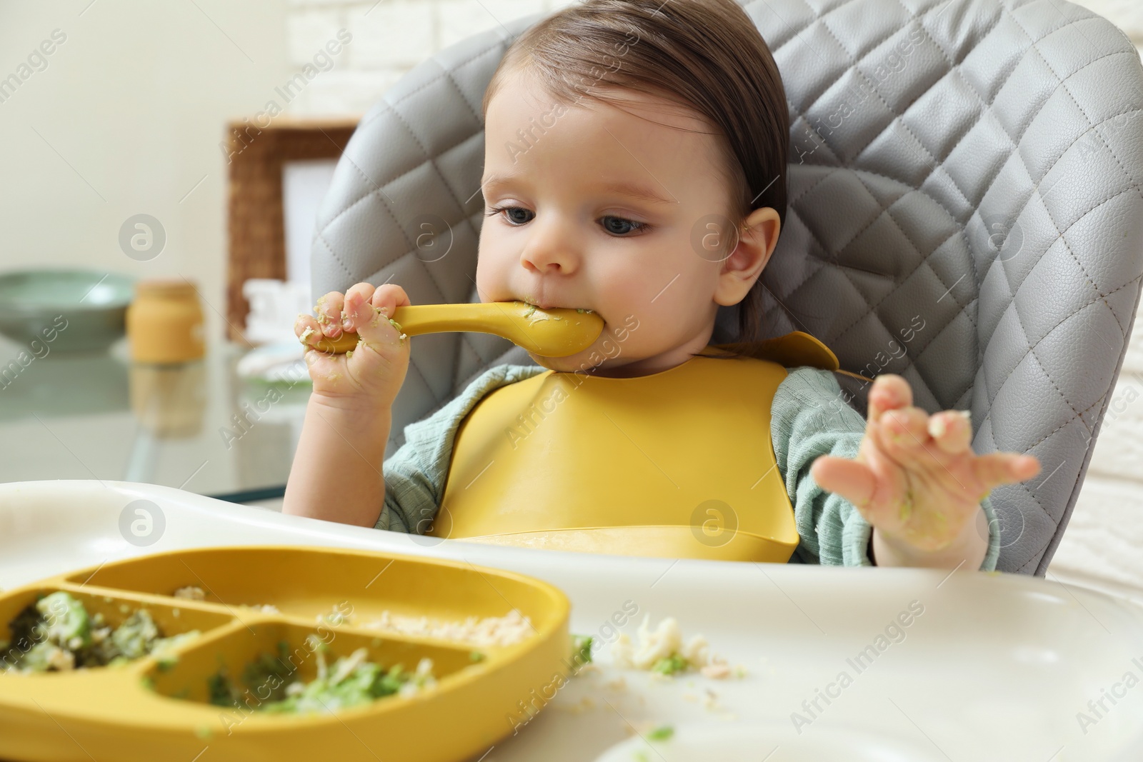 Photo of Cute little baby eating healthy food in high chair indoors