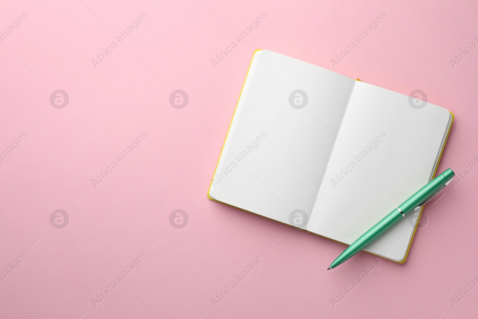 Photo of Open notebook with blank pages and pen on light pink background, top view. Space for text