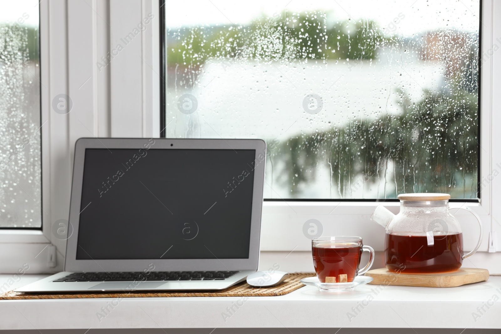 Photo of Modern laptop and tea on white sill near window