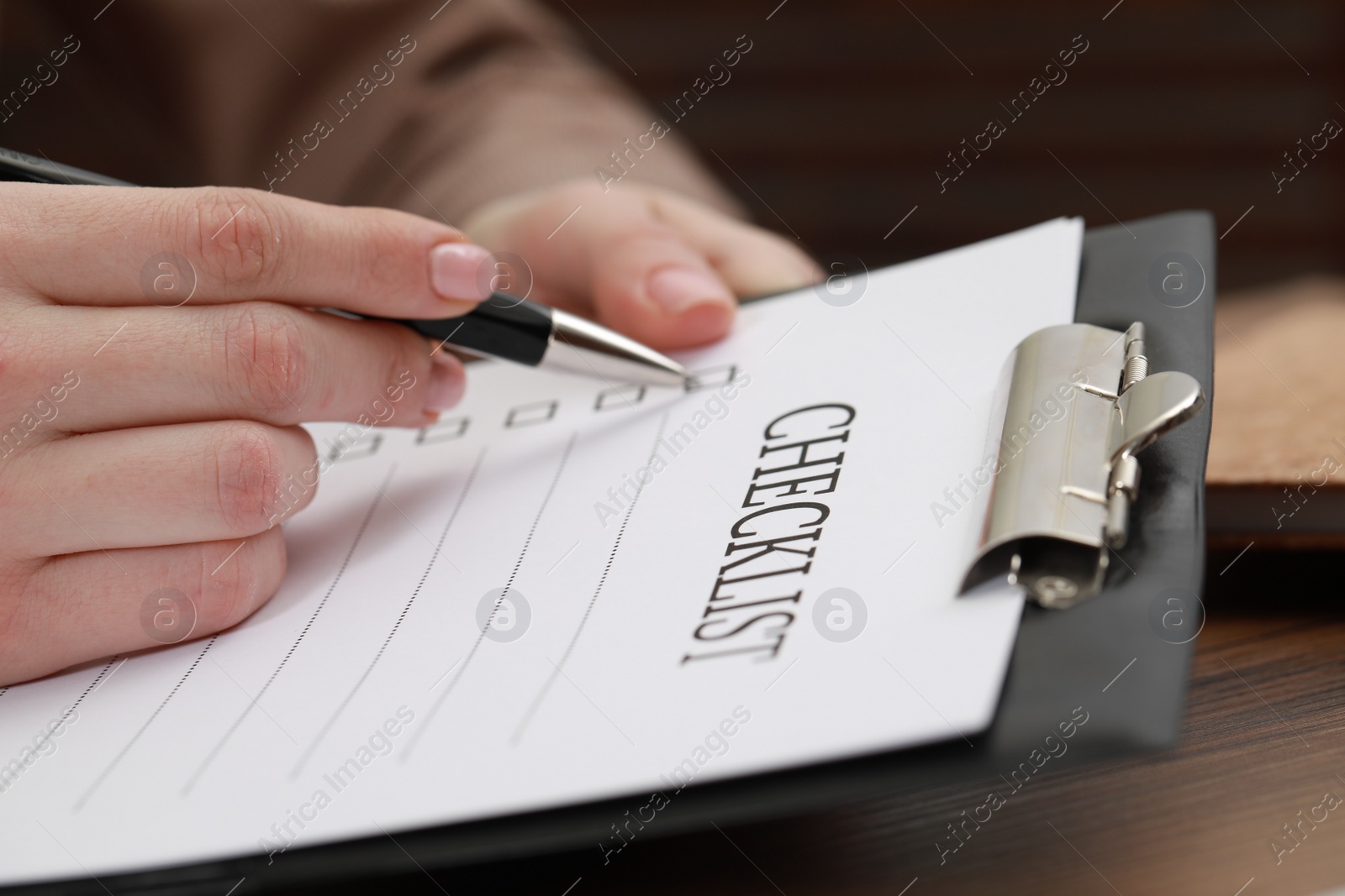 Photo of Woman filling Checklist at wooden table, closeup