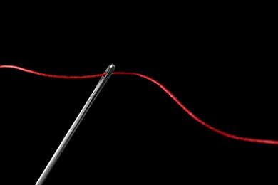 Photo of Sewing needle with red thread on black background