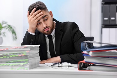 Photo of Overwhelmed man sitting at table with stacks of documents and folders in office