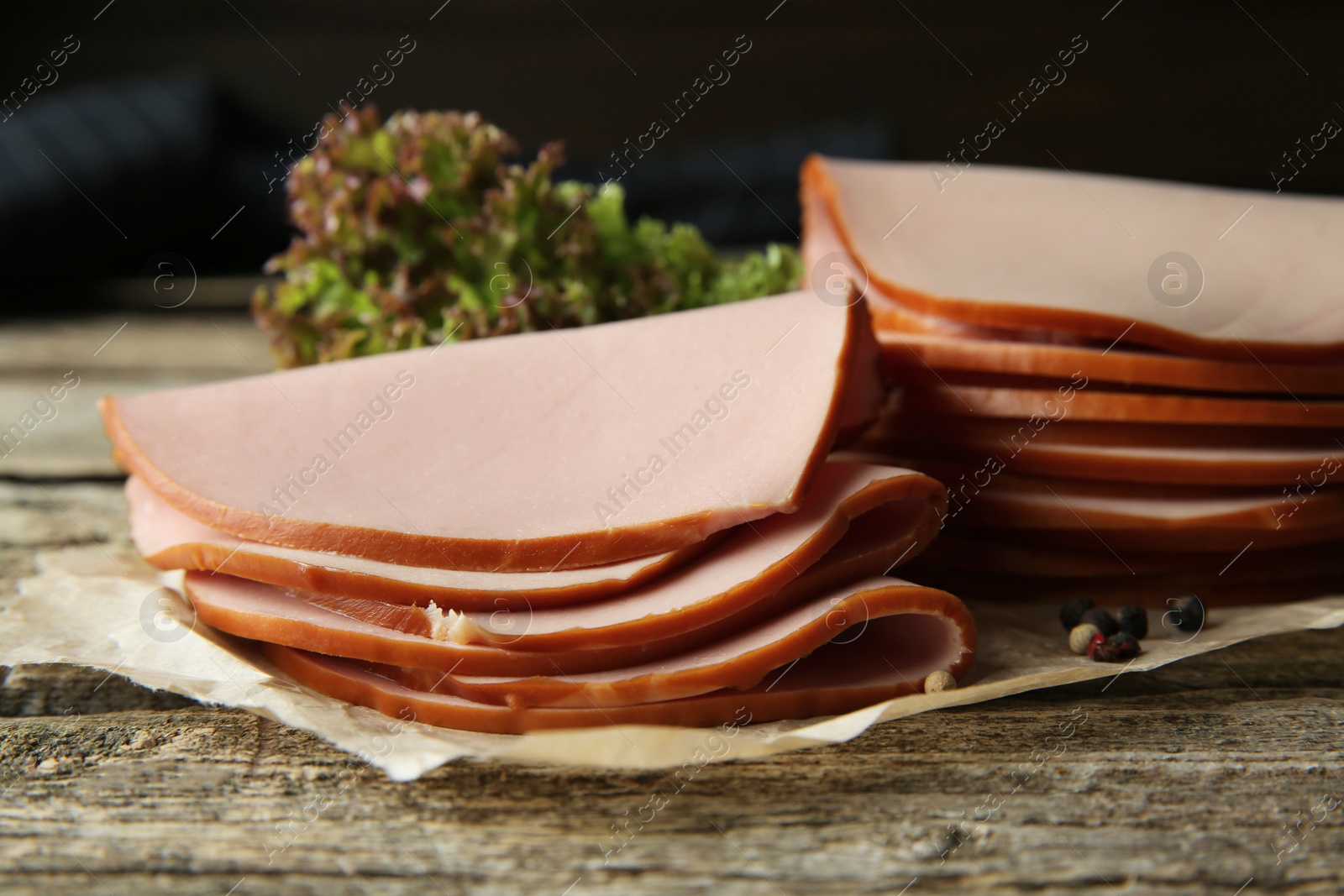 Photo of Slices of delicious boiled sausage with lettuce and spices on wooden table, closeup