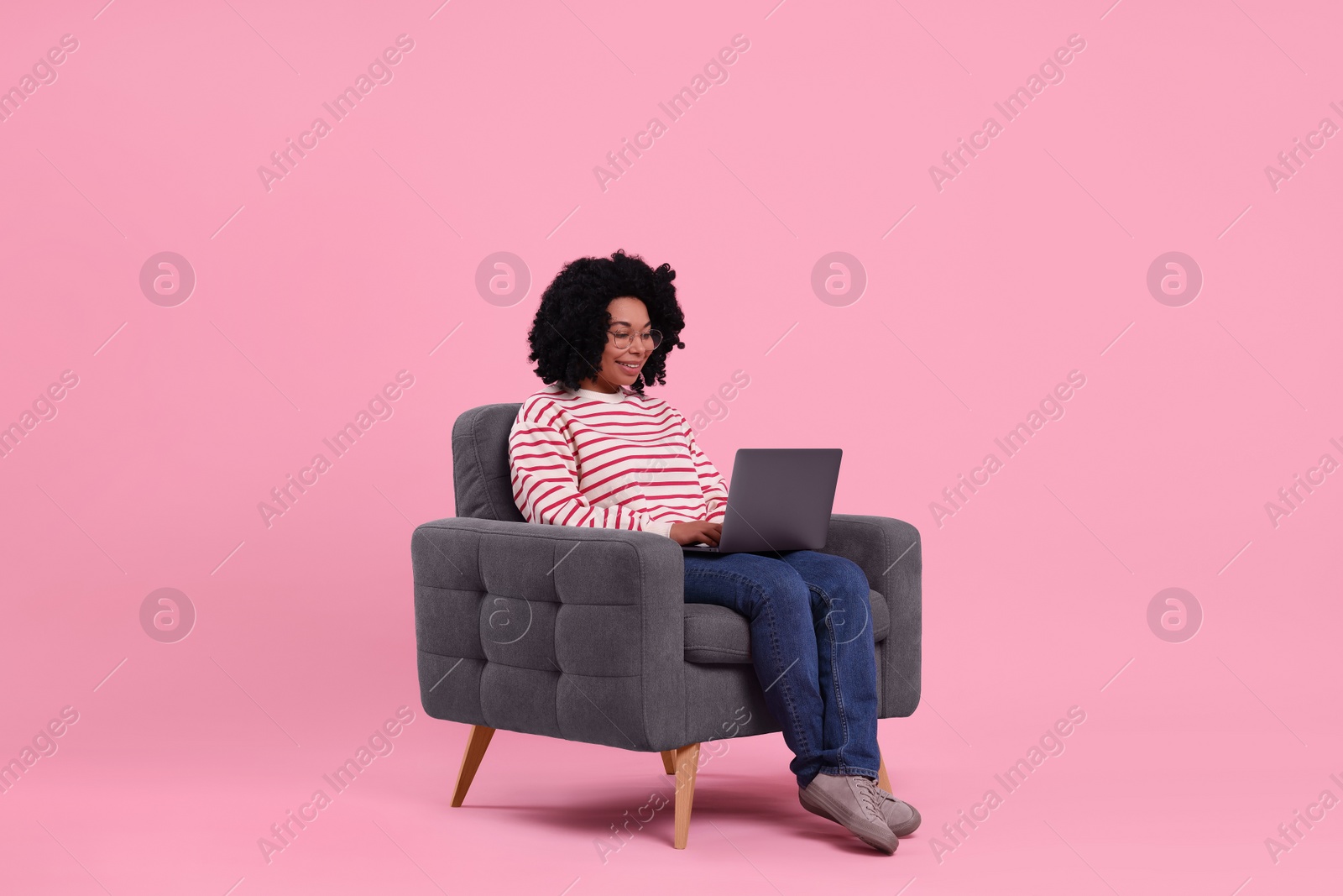 Photo of Happy young woman with laptop sitting in armchair against pink background