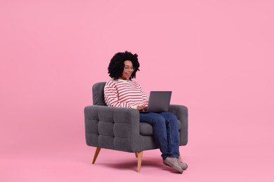 Photo of Happy young woman with laptop sitting in armchair against pink background