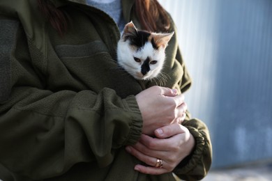 Photo of Soldier in uniform warming little stray cat on blurred background, closeup