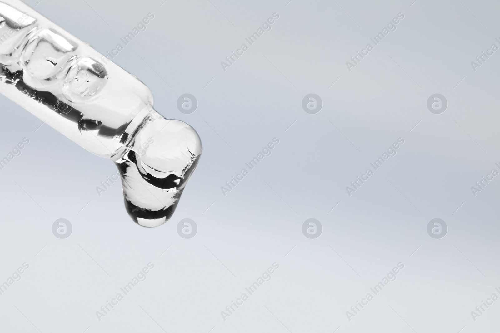 Photo of Dripping face serum from pipette on white background, closeup. Space for text