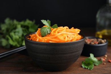 Photo of Delicious Korean carrot salad with parsley in bowl on wooden table