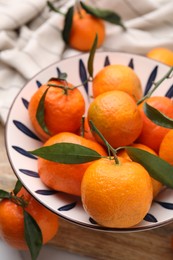 Photo of Fresh ripe tangerines with green leaves in bowl on table, above view