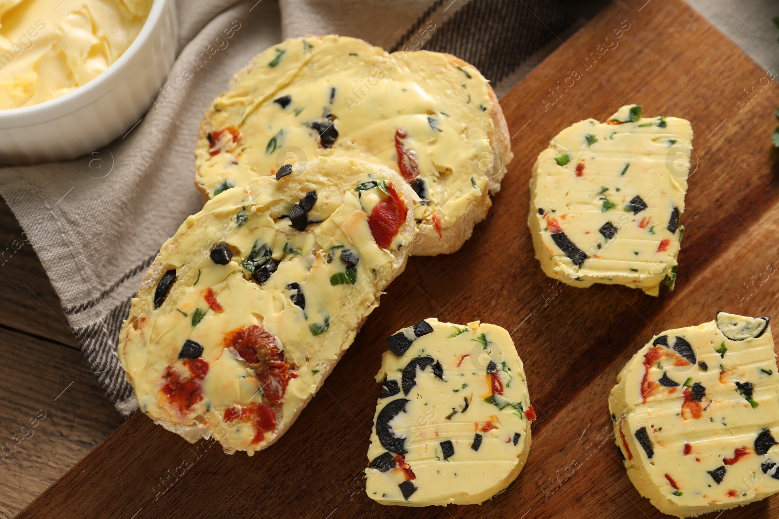 Photo of Tasty butter with olives, chili pepper, parsley and bread on wooden table, top view