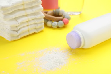 Bottle, scattered dusting powder and diapers on yellow background. Baby care products