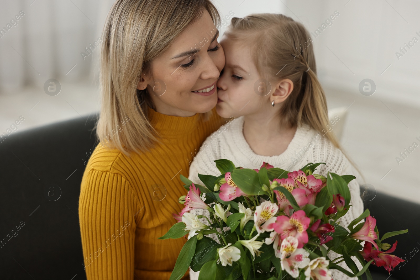 Photo of Little daughter kissing and congratulating her mom with bouquet of alstroemeria flowers at home. Happy Mother's Day