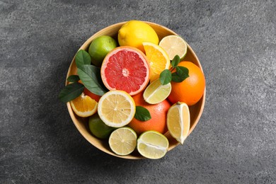 Photo of Different fresh citrus fruits and leaves in bowl on grey textured table, top view