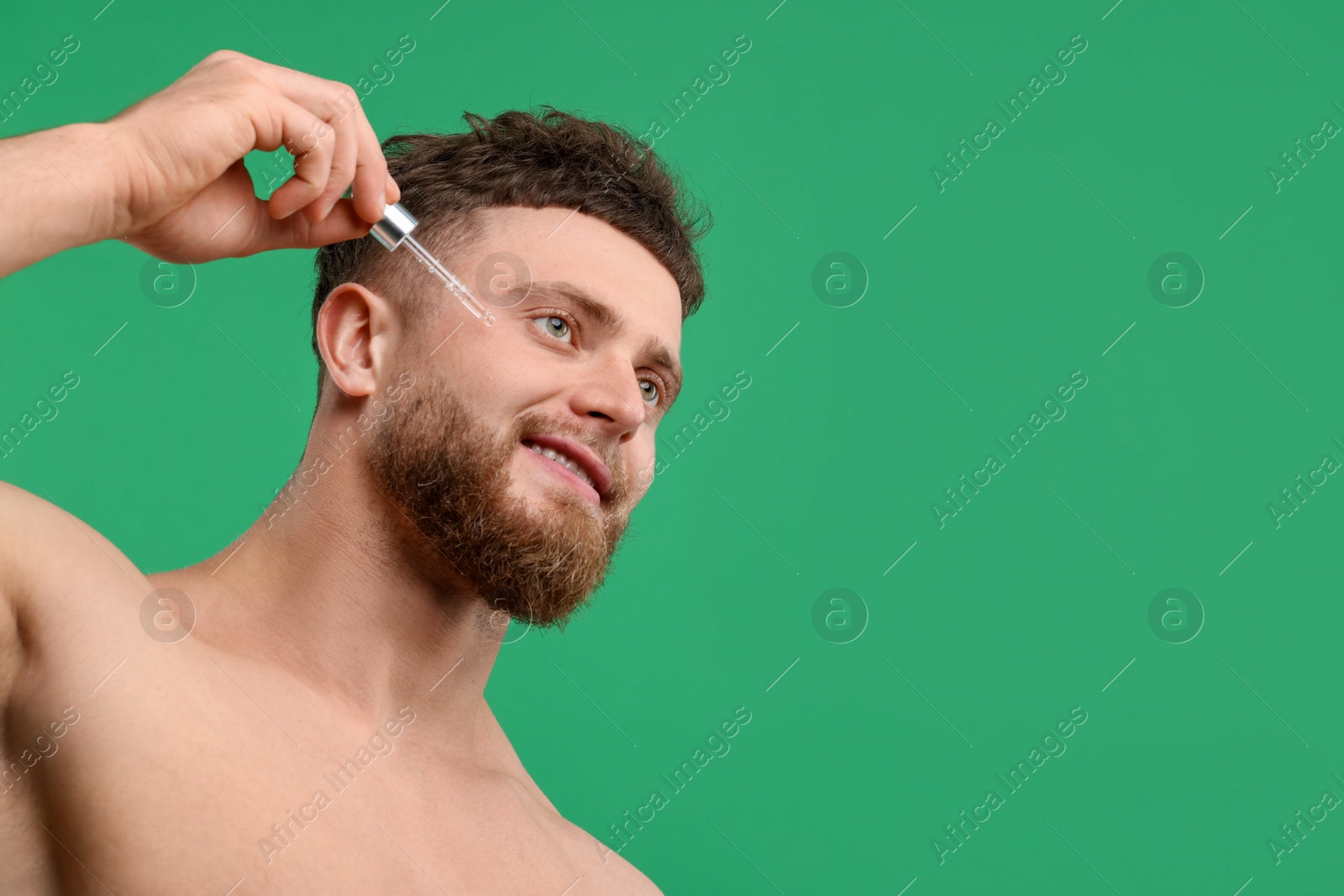 Photo of Handsome man applying serum onto his face on green background, space for text