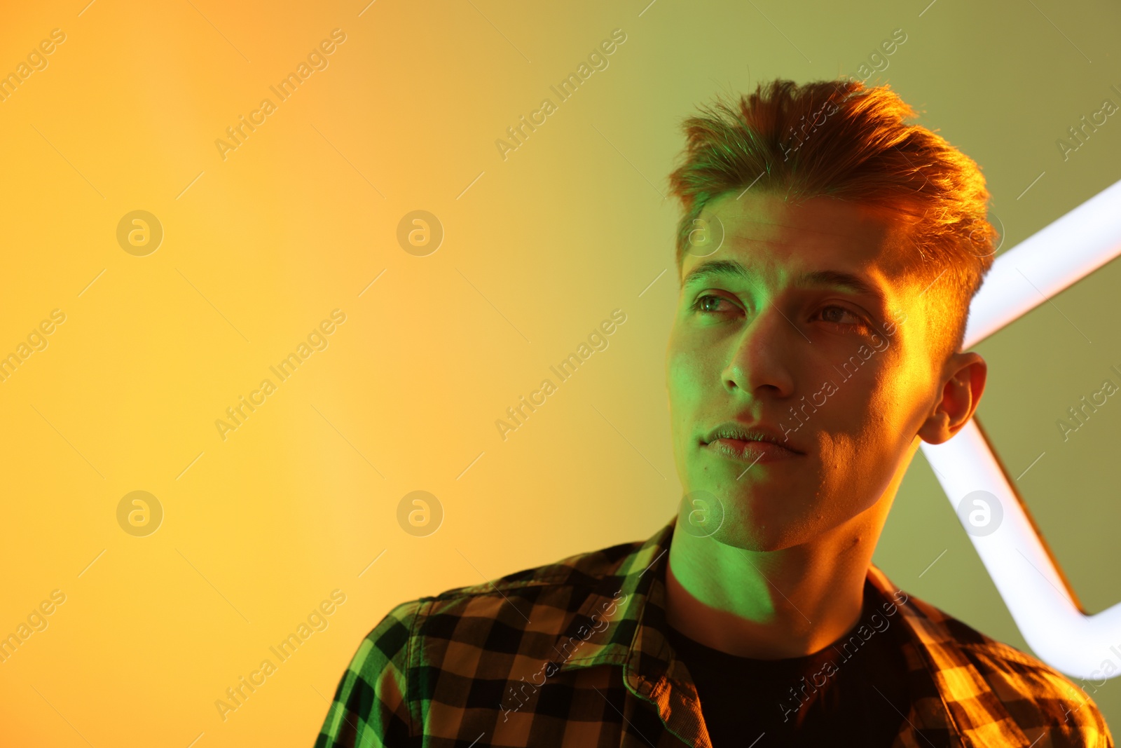 Photo of Young man with square lamp on color background in neon lights. Space for text