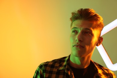 Young man with square lamp on color background in neon lights. Space for text