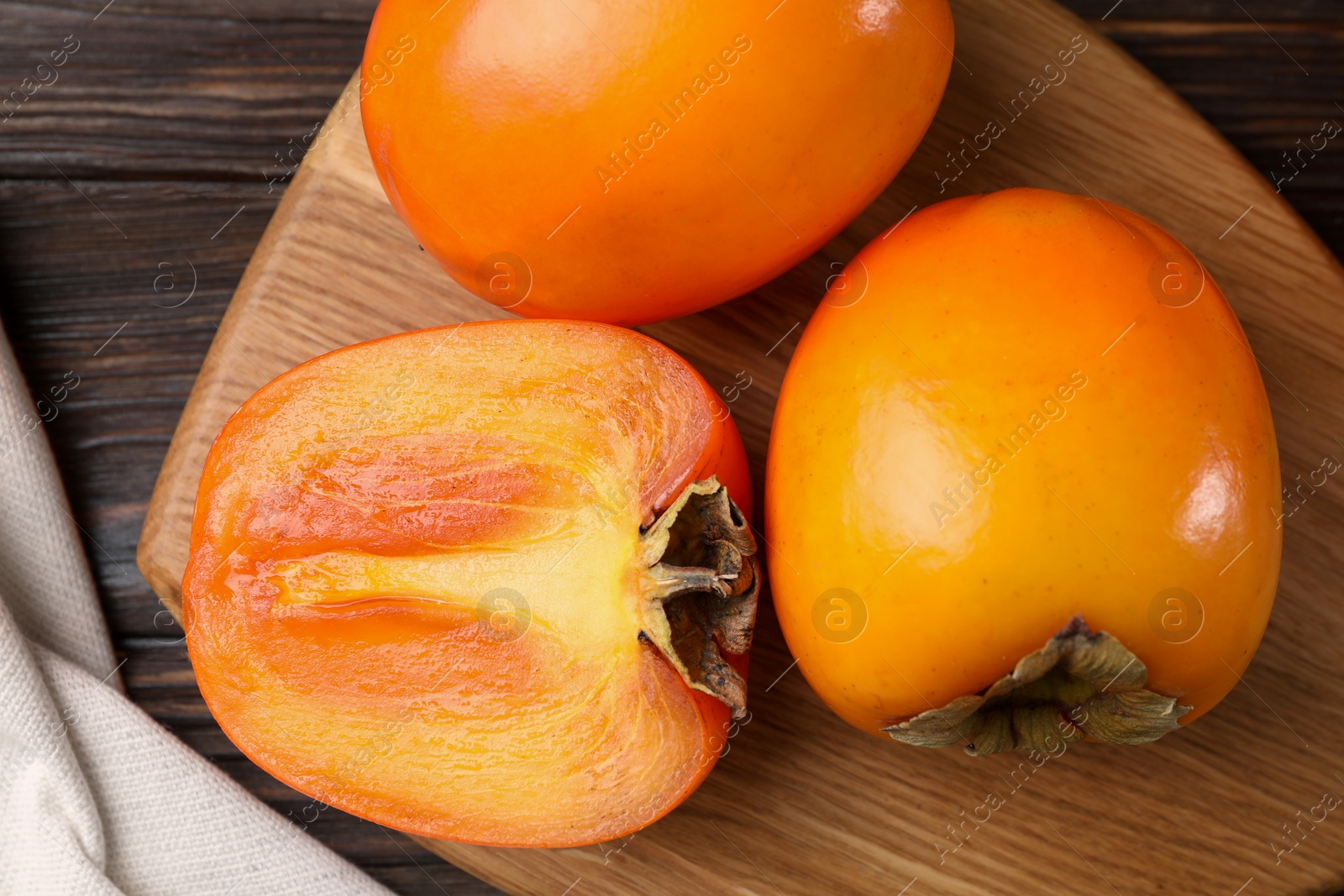 Photo of Whole and cut delicious ripe persimmons on wooden table, top view