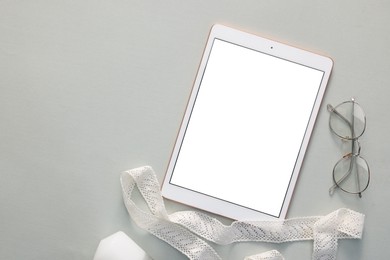 Photo of Modern tablet, glasses and ribbon on light grey background, flat lay. Space for text