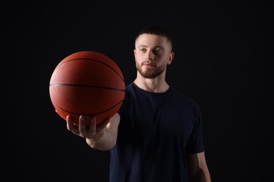 Athletic young man with basketball ball on black background, selective focus