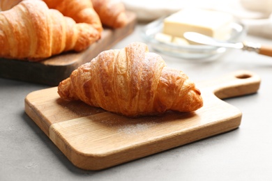 Photo of Wooden board with tasty croissant on grey table. French pastry