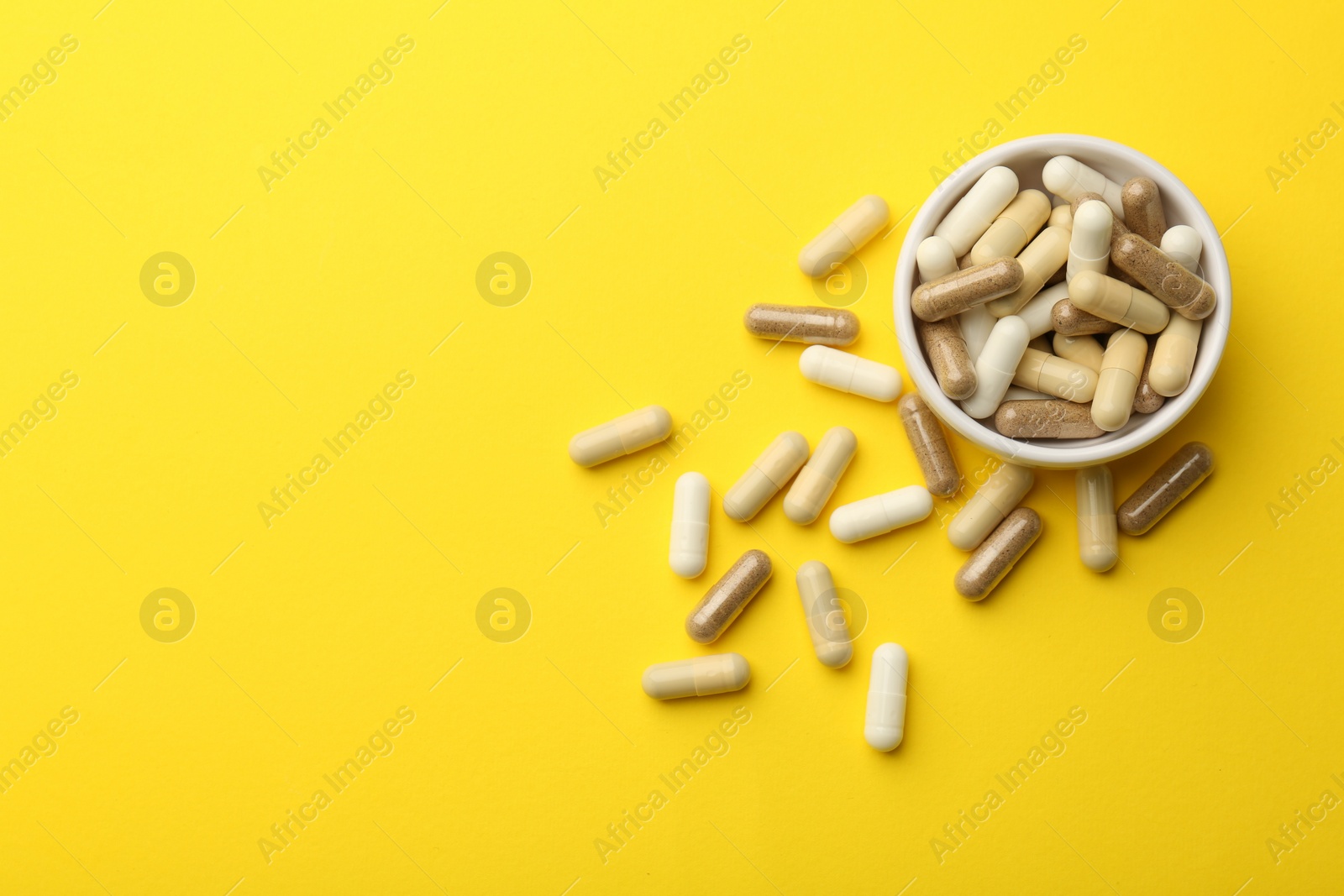 Photo of Different vitamin capsules on yellow background, flat lay. Space for text