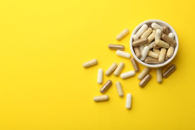Photo of Different vitamin capsules on yellow background, flat lay. Space for text